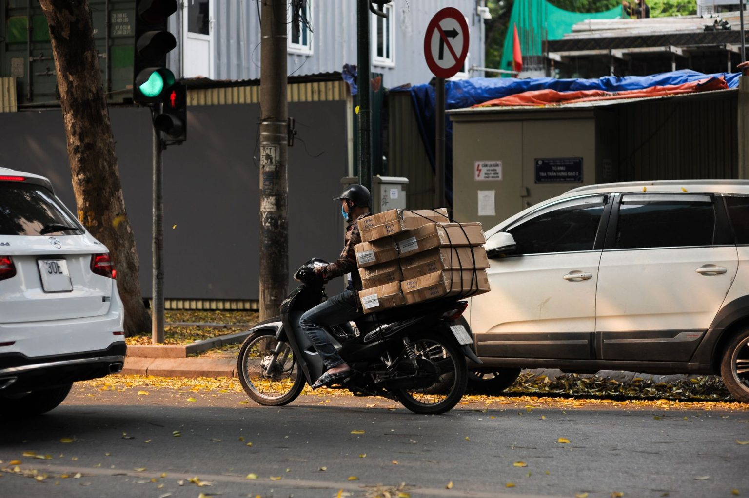Motociclista profissional com caixas empilhadas aguarda o sinal abrir em uma rua movimentada da cidade.