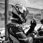 Motociclista com equipamento de proteção ajusta o capacete ao ar livre.