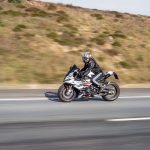 Motociclista usando capacete conduz uma motocicleta esportiva em uma rodovia de pista aberta.